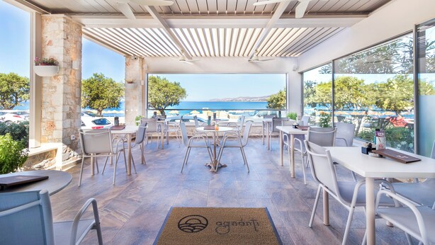 Un área de estar al aire libre con mesas y sillas, vista al mar y un pilar de piedra.