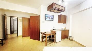 A compact hotel room with a bed, a small kitchenette, a wooden desk, and a television.