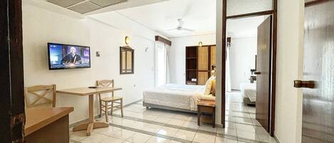 A hotel room with a bed, a desk, a chair, a television, and a bathroom visible through an open door.