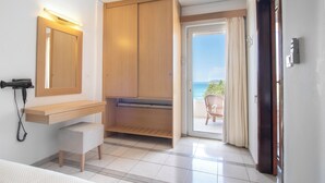 Habitación de hotel con armario de madera, mesita de noche, una silla y vista al mar a través de un ventanal corredero.