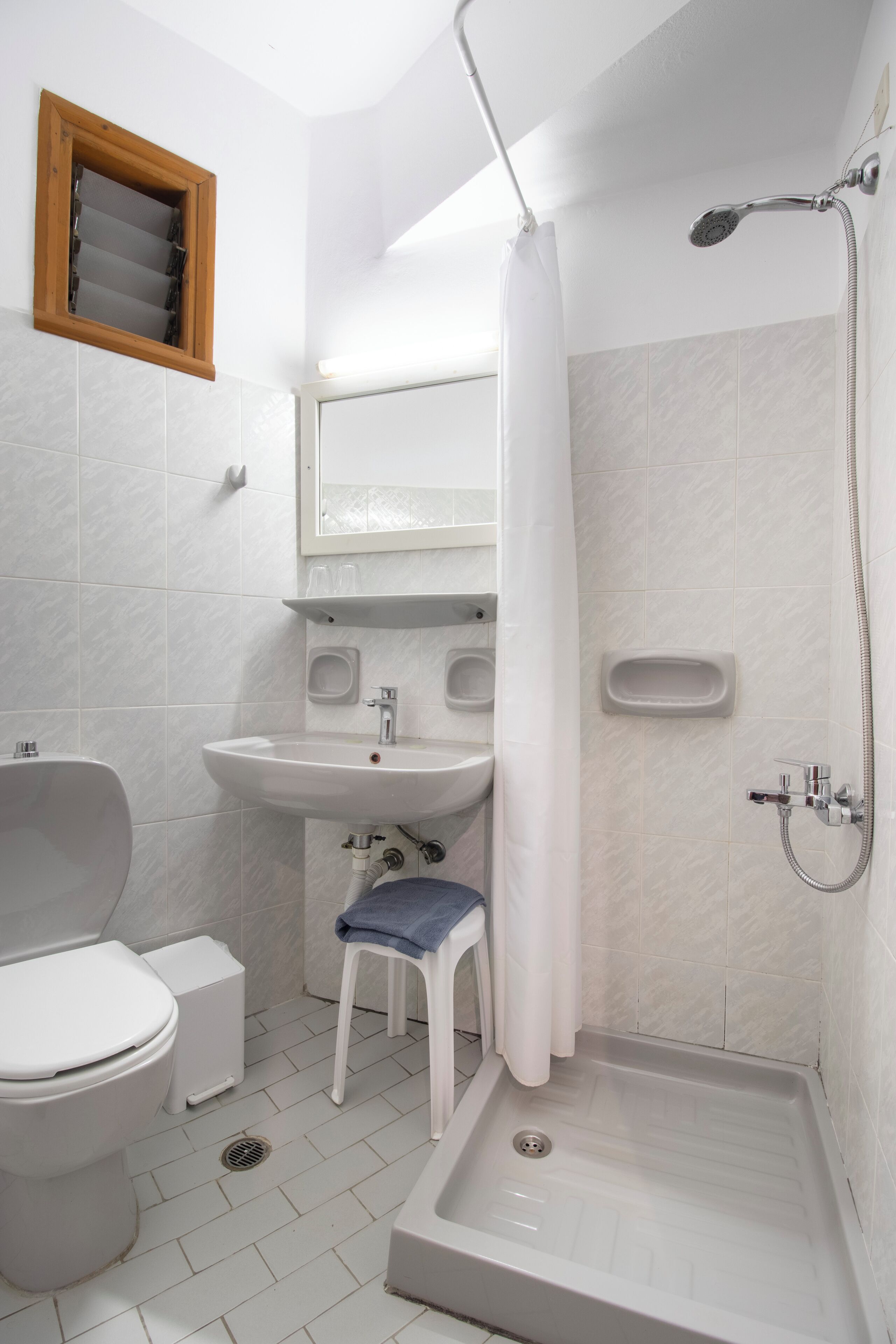 A bathroom with a toilet, sink, shower, and a small stool.