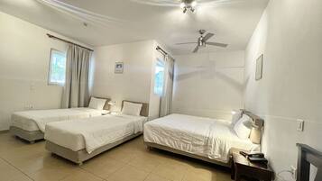 A hotel room with two single beds, a ceiling fan, a desk with a chair, and a TV.