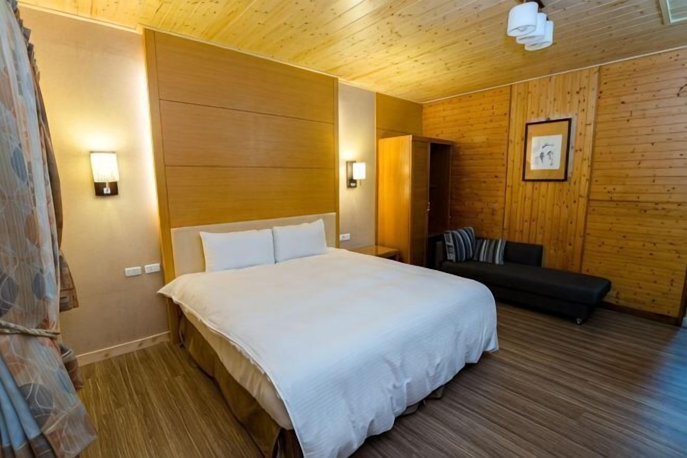 A bedroom with a bed, a sofa, wooden walls, and two wall-mounted lights.