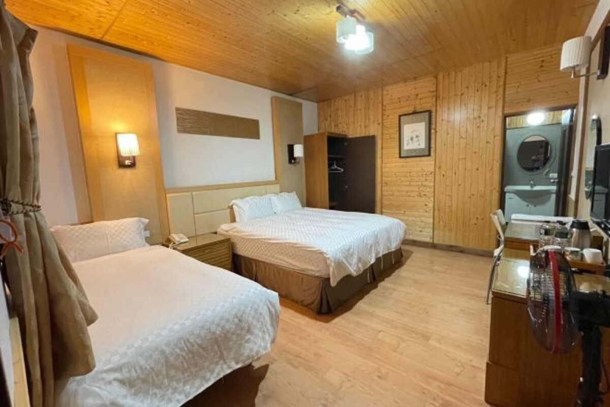Ein Hotelzimmer mit zwei Betten, Holzwänden, einem Spiegel, einem Waschbecken und einem Ventilator.
