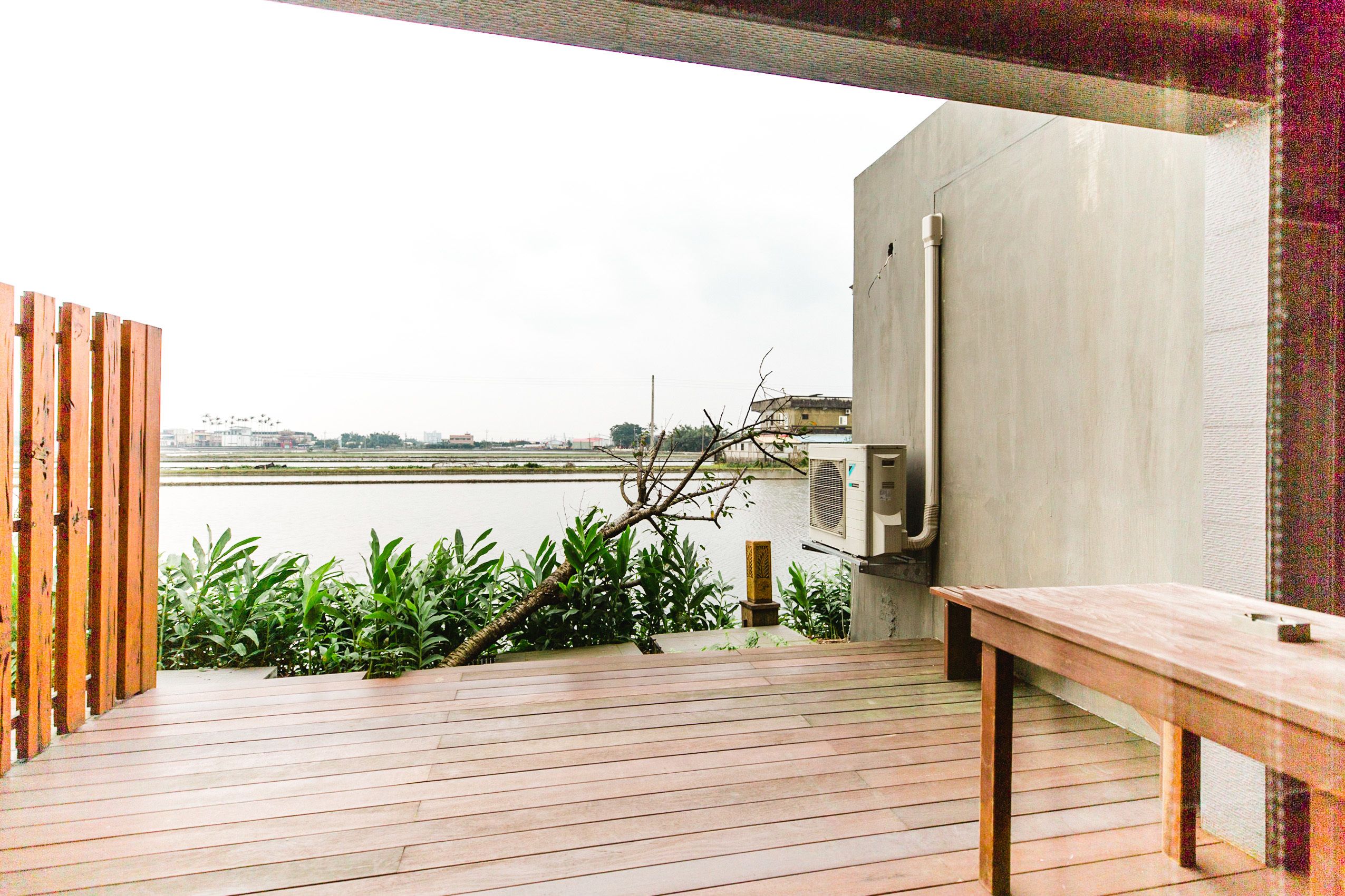A wooden deck with a bench, overlooking a body of water and a cityscape.