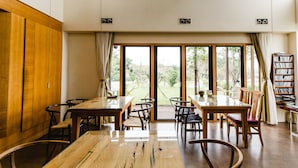 A dining area with a wooden table and chairs, large windows with curtains, and a bookshelf. - Serene Gray (Wujie)