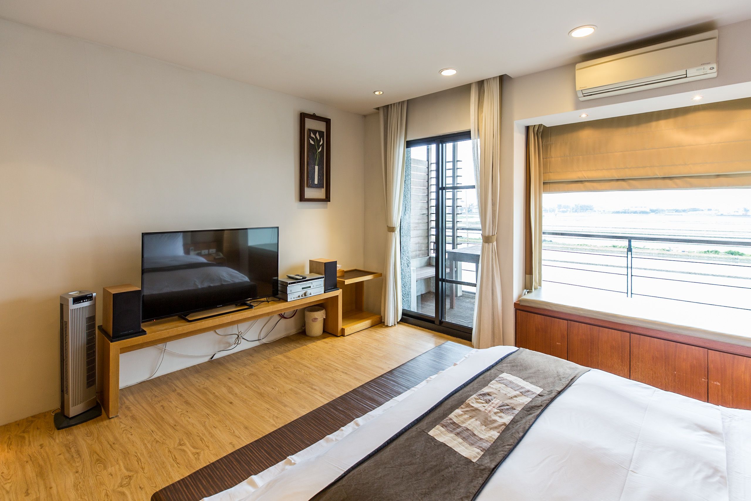 Habitación de hotel con cama, televisor, parlante y ventana con vista al exterior.