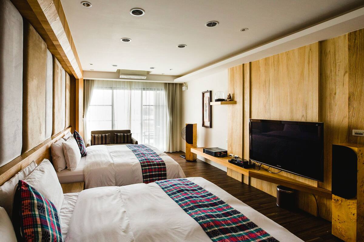 A hotel room with two beds, a TV, a small table, and a window with curtains.