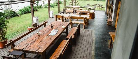 An outdoor wooden deck with picnic tables and benches, surrounded by greenery and a view of a body of water.