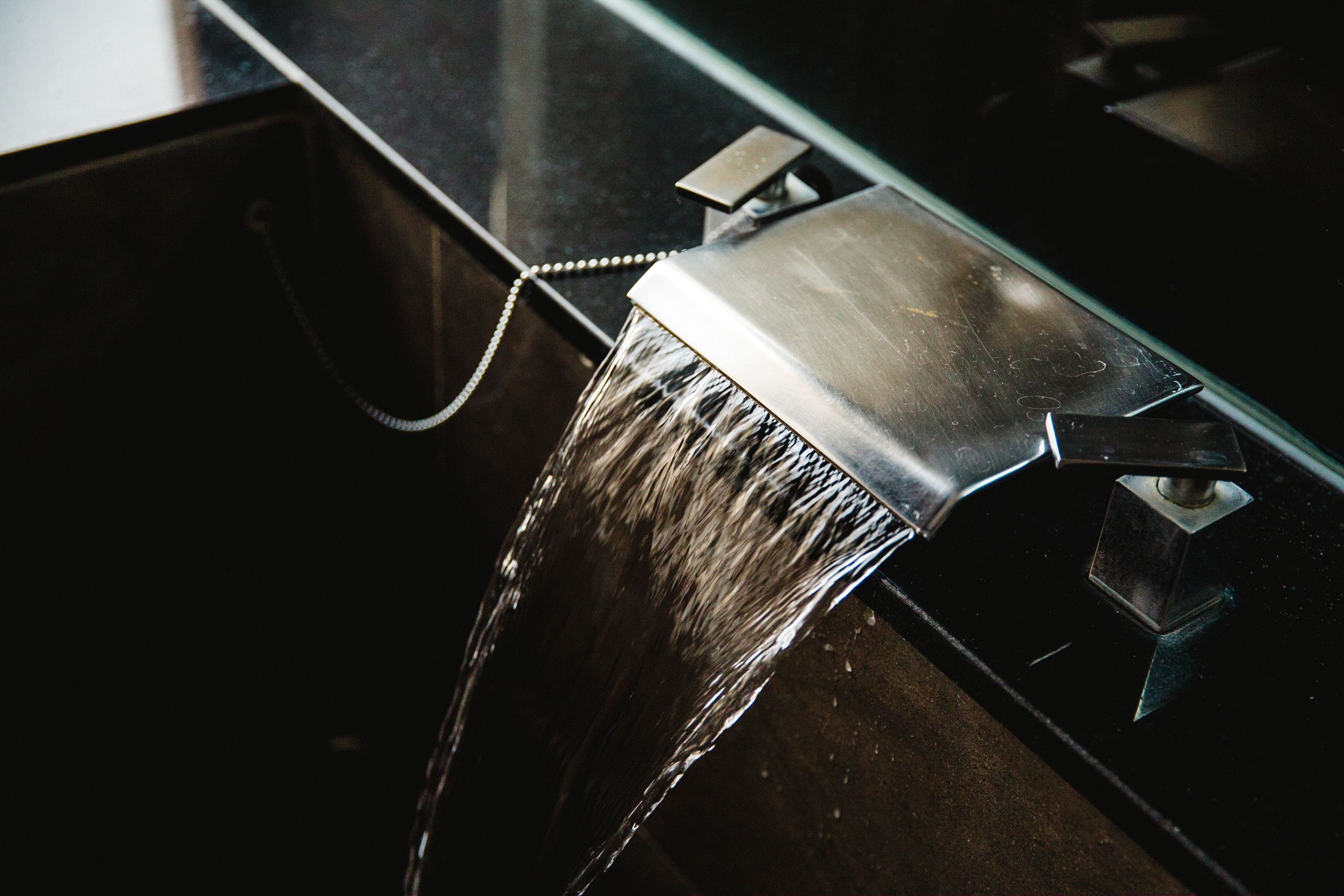 Un baño moderno con un lavamanos de acero inoxidable y un grifo abierto.