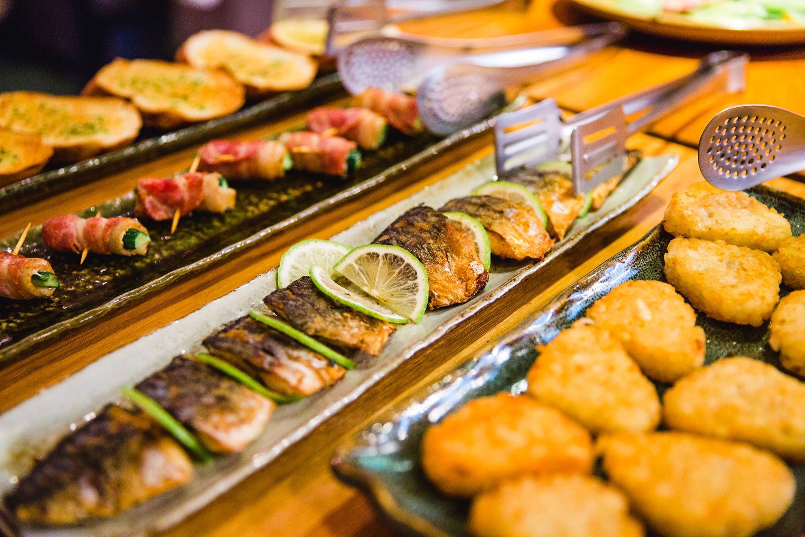 Un bufé con diversos platos, incluyendo carnes a la parrilla, pescado asado y frituras.