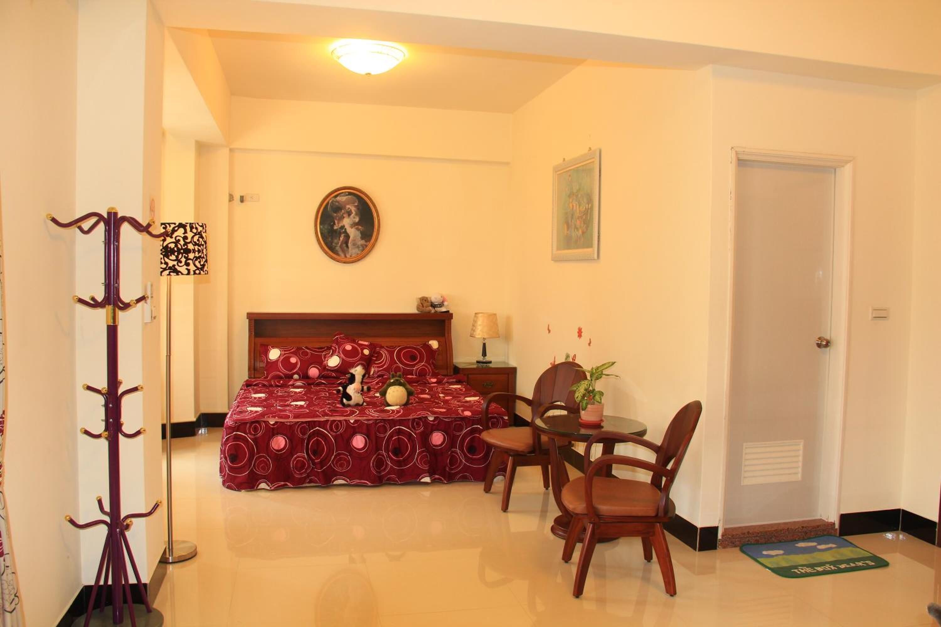 A bedroom with a bed, a bedside table, a lamp, a chair, a dining table, and a coat rack.