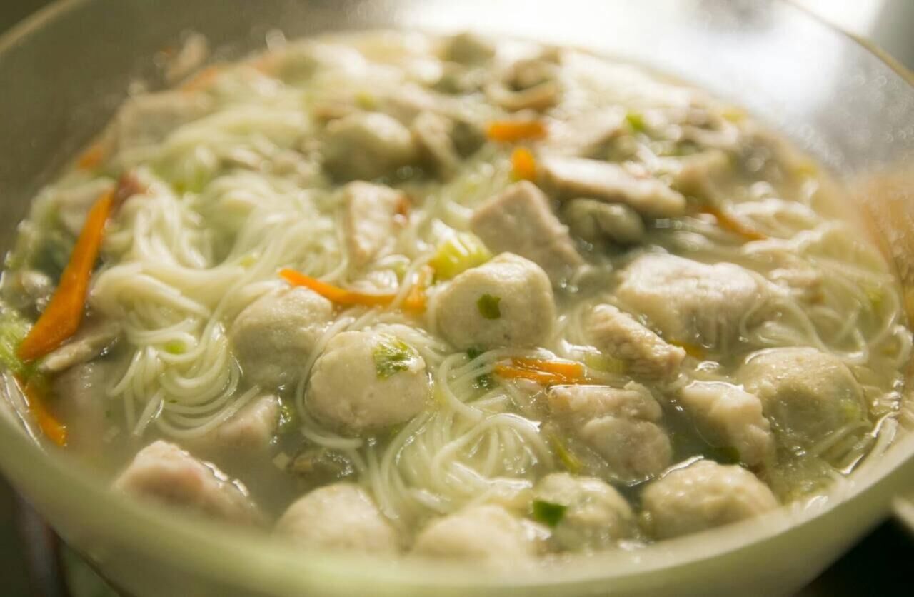 A bowl of soup with noodles, meatballs, and vegetables.