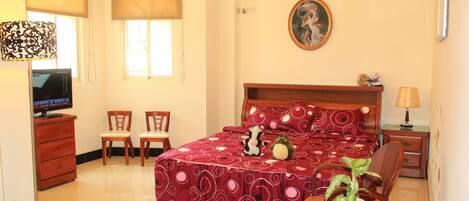 Una habitación de hotel con cama, escritorio, silla, televisor, lámpara y planta en maceta.