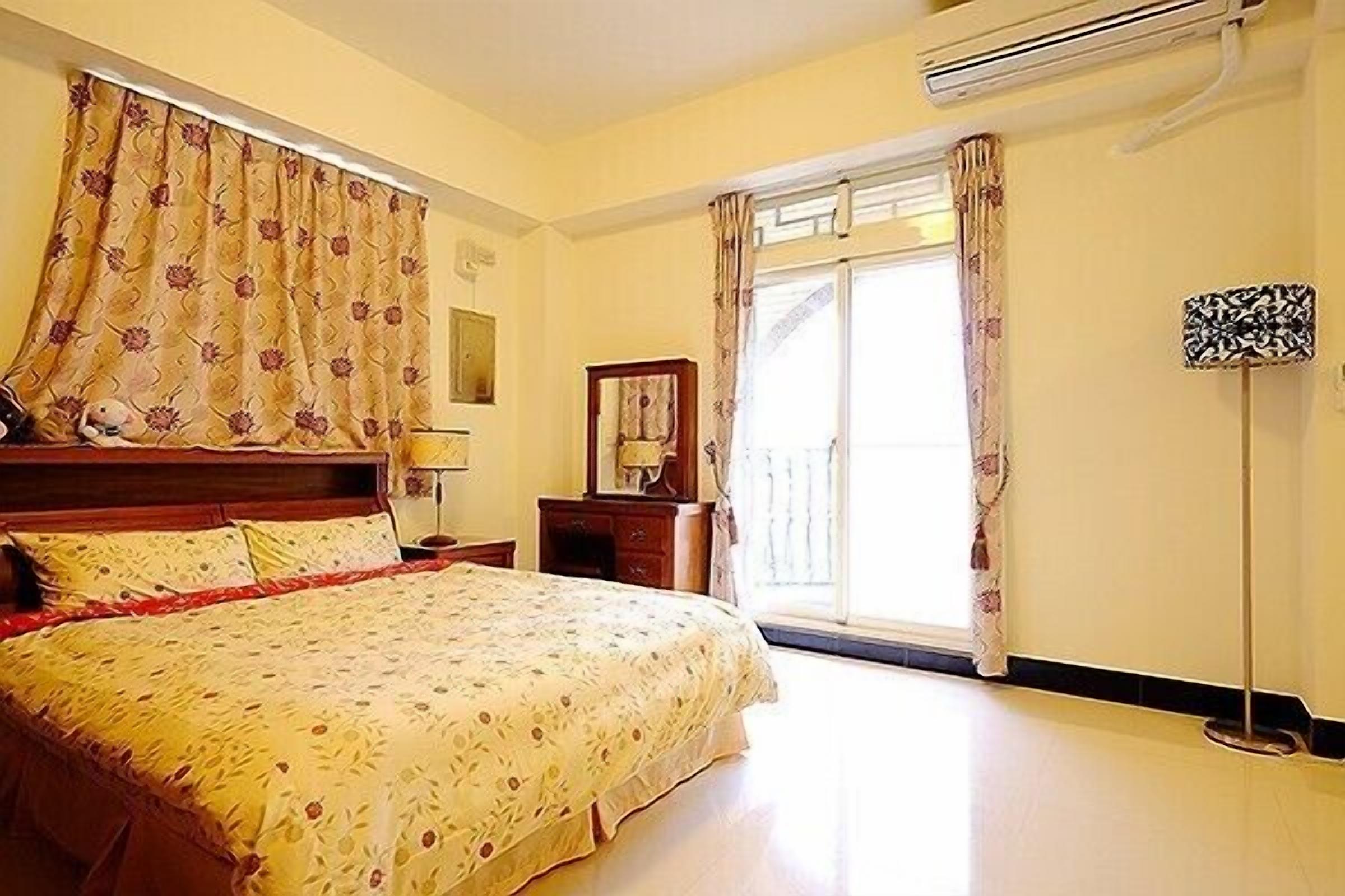 A bedroom with a bed, a nightstand, a dresser, a mirror, and a window with curtains.