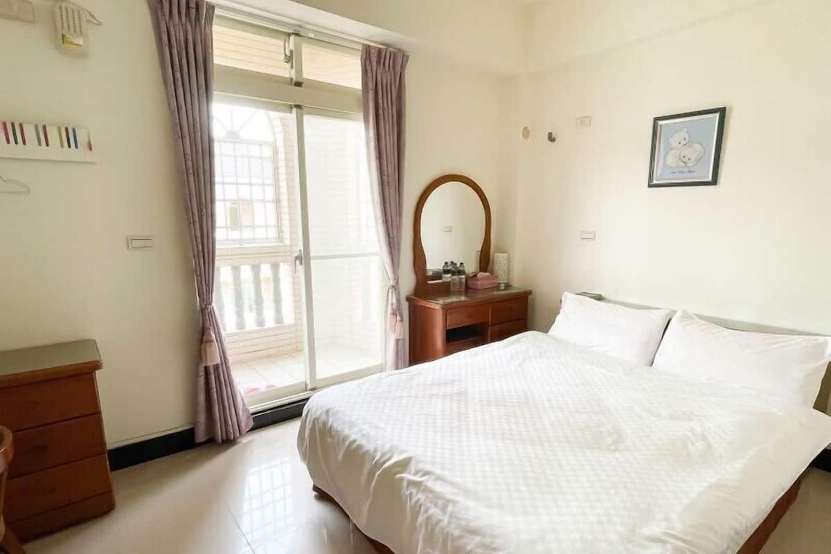 A hotel room with a bed, a wooden dresser, a mirror, and a window with curtains.