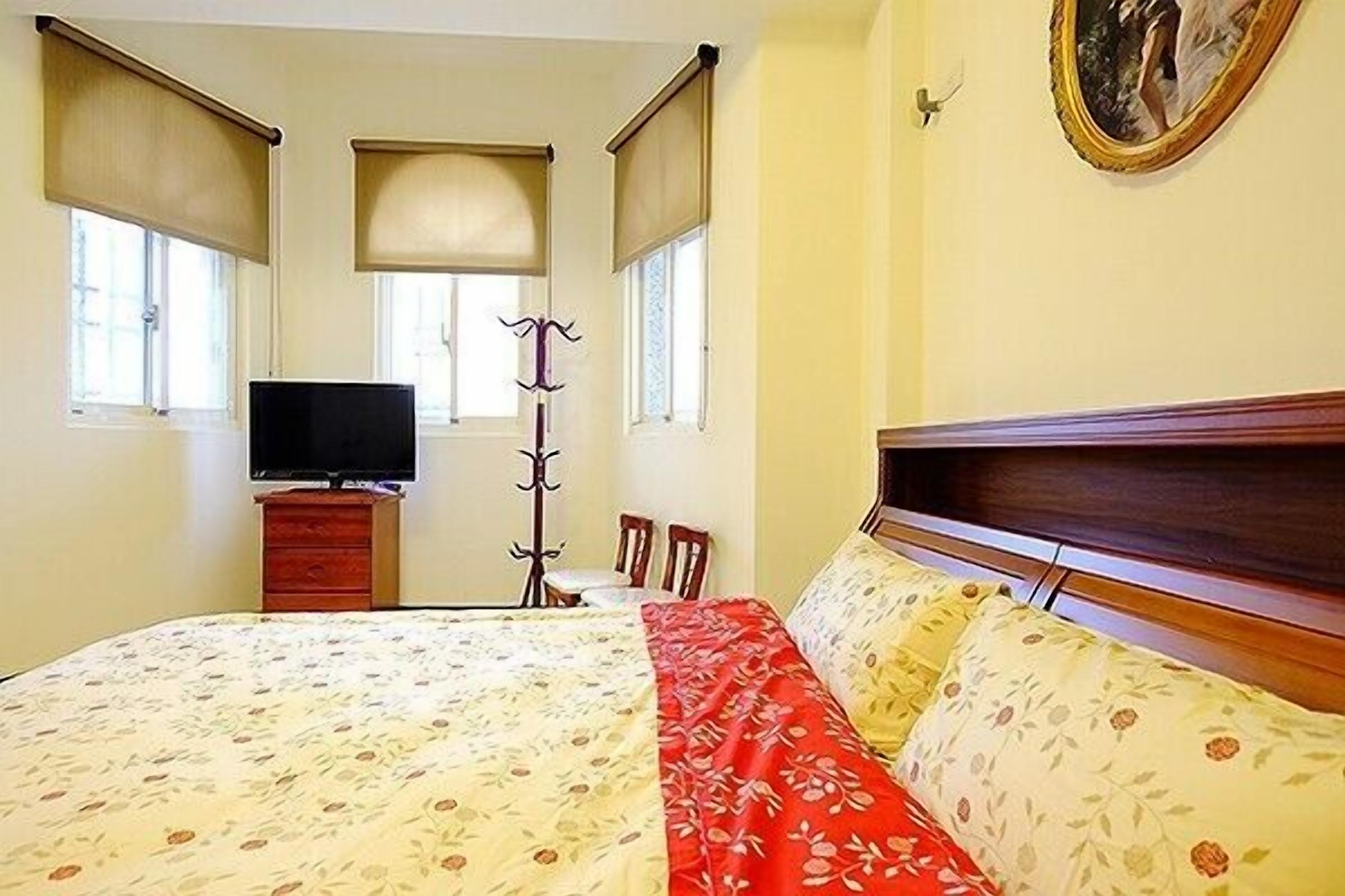A bedroom with a bed, a television, a coat rack, and a window with a view.