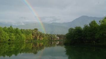 A tranquil lake with a rainbow, surrounded by lush greenery and mountains.