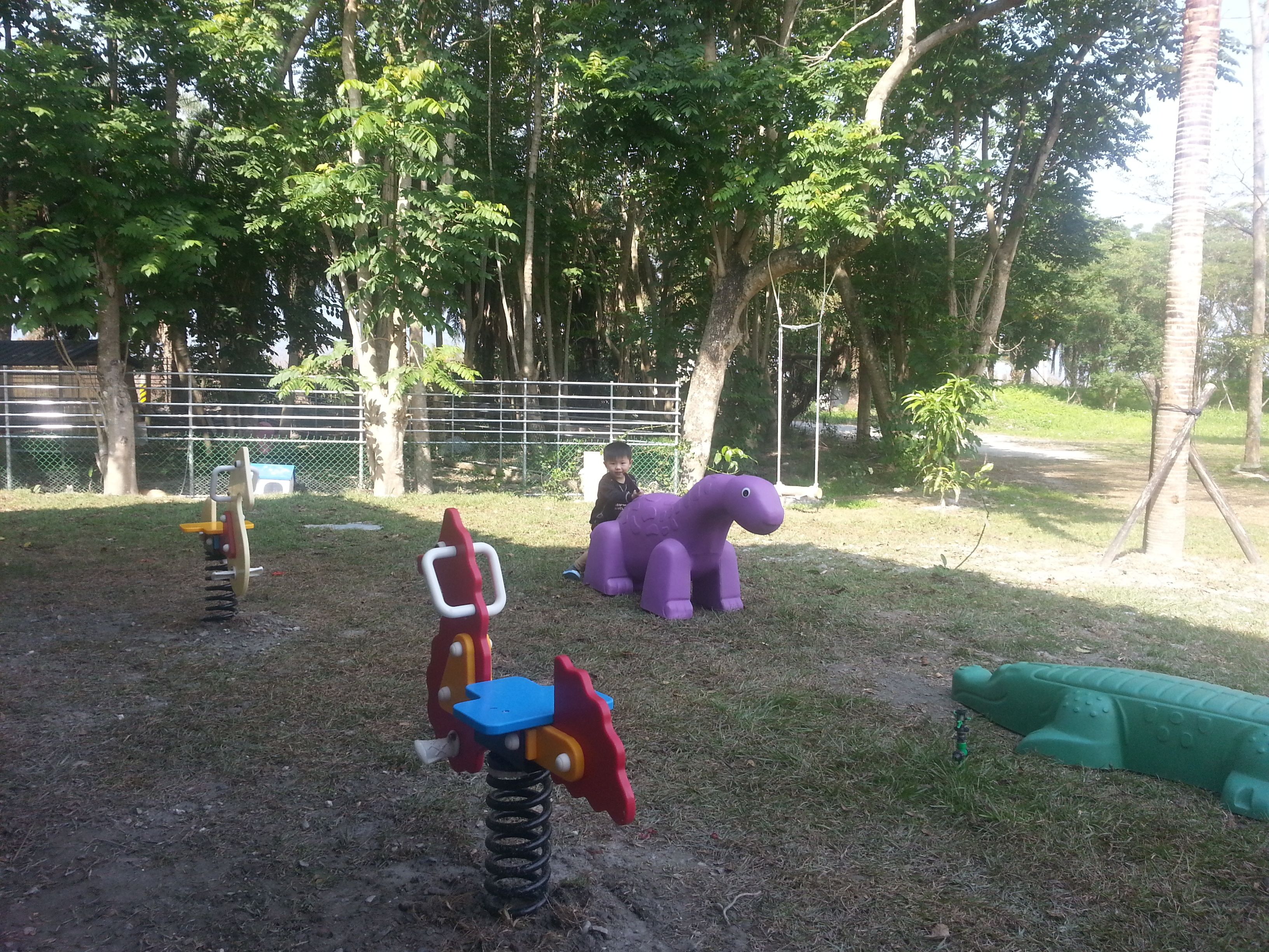 Un parque infantil con un sube y baja, un dinosaurio morado y un tobogán verde.