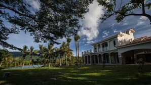 A large, white building with a tiled roof and arched windows, surrounded by palm trees and a body of water. - Villa of Permaculture (Shoufeng)