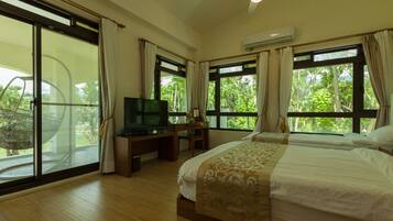 Habitación de hotel con cama, escritorio con televisor y grandes ventanales que dan a zonas verdes.