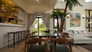 A modern living room with a glass dining table, wooden chairs, a sofa, and a large window with curtains. - Villa of Permaculture (Shoufeng)