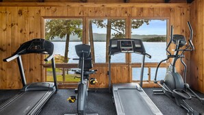 Una palestra con tre tapis roulant e un ellittica, pareti in legno e vista su un lago.