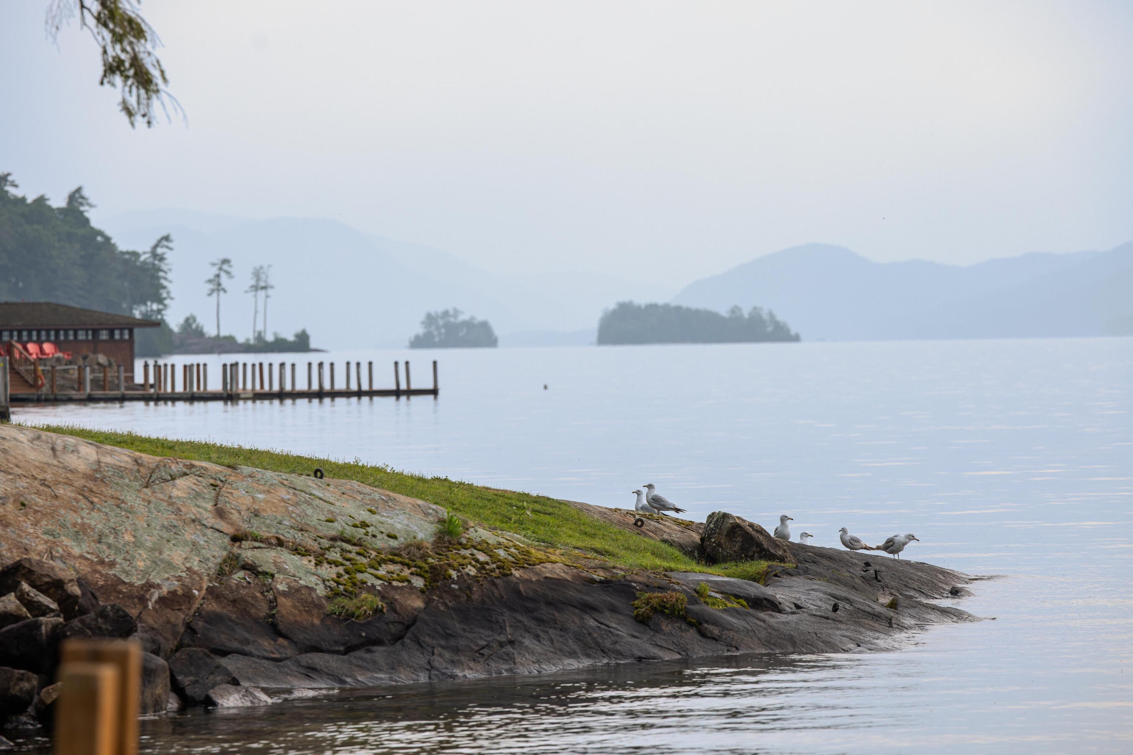 Vista de un lago con un muelle que se adentra en aguas tranquilas, rodeado de costas rocosas y montañas a lo lejos.