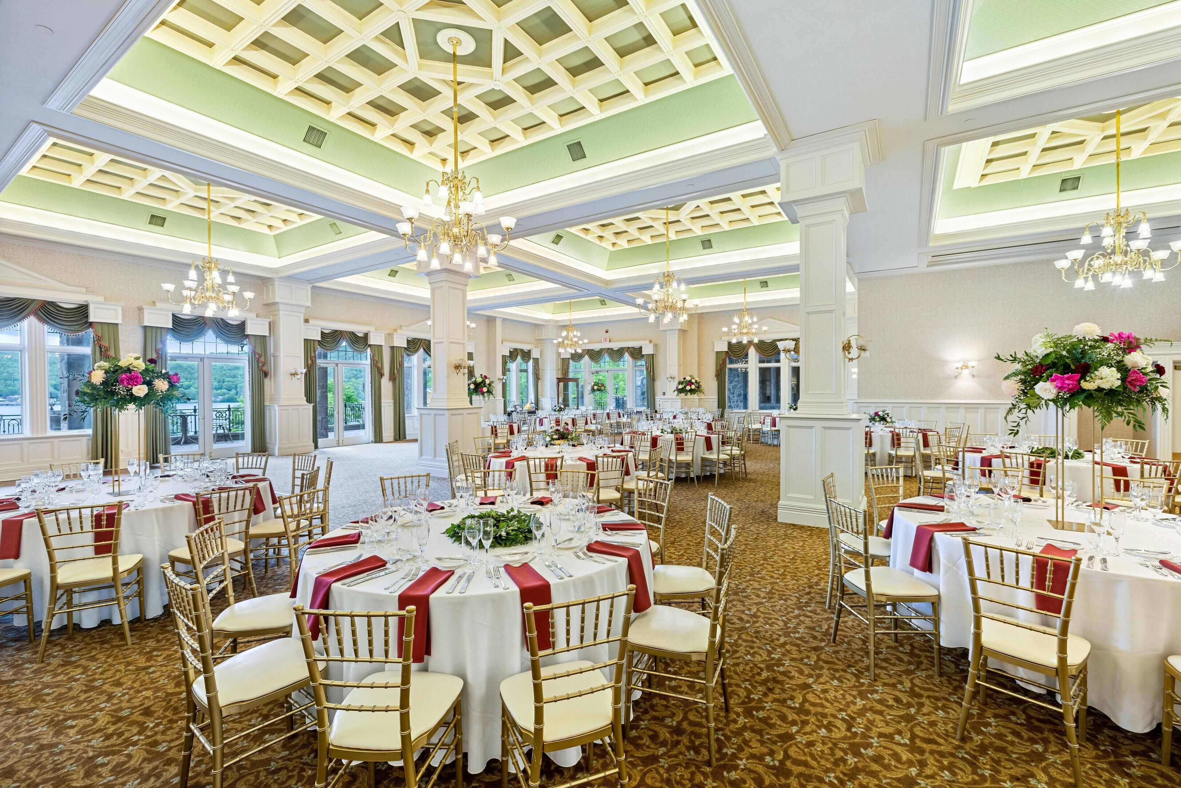 A banquet hall with round tables, gold chairs, and chandeliers.