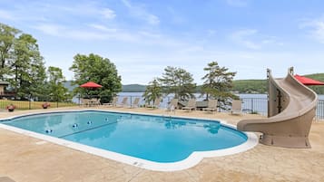 A swimming pool with a slide, lounge chairs, and a view of a lake.