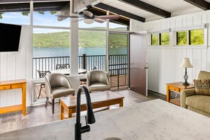 A spacious balcony with a view of a lake, furnished with a table, chairs, and a TV mounted on the wall. - Sun Castle Resort (Lake George)