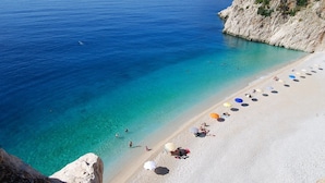 A beach with clear turquoise water, a sandy shore, and a rocky cliff. - Soothe Hotel (Kas)