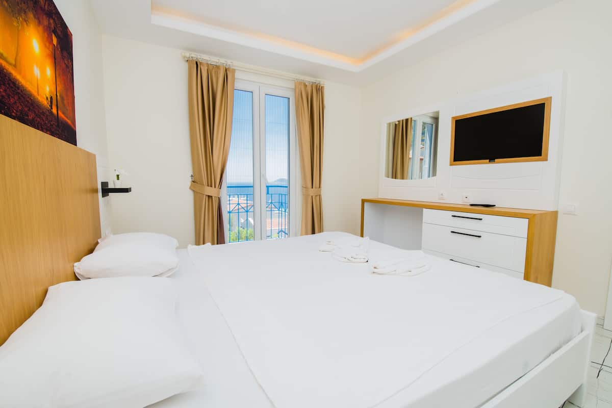 Une chambre d’hôtel avec un grand lit, un téléviseur fixé au mur, un bureau avec des tiroirs et une fenêtre avec des rideaux.