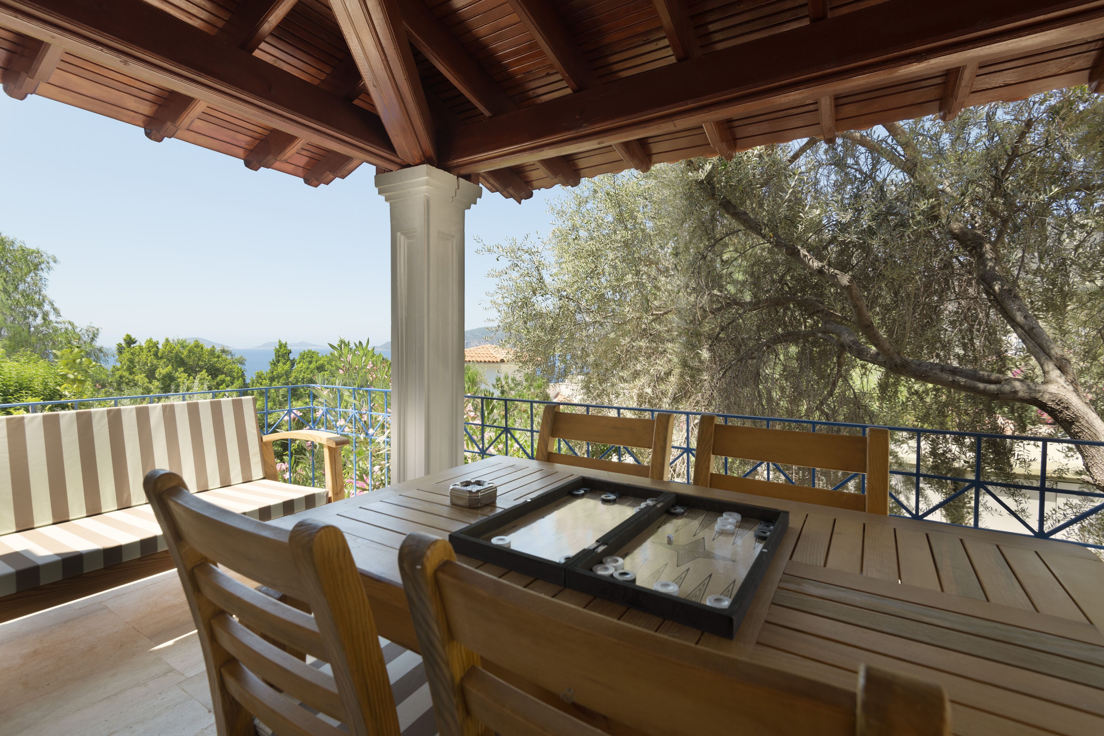 A wooden table and chairs under a pergola with a view of trees and mountains.