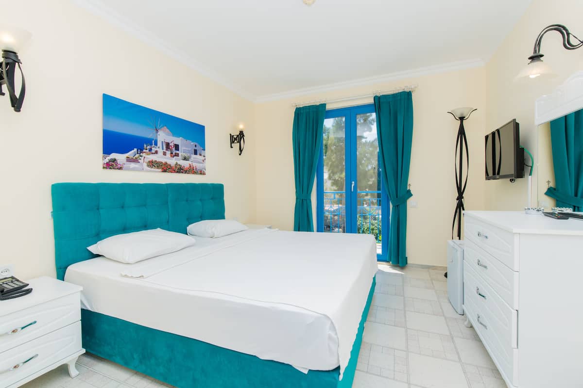 Une chambre avec un grand lit, une commode blanche, un tableau représentant un paysage côtier et une vue à travers une porte.