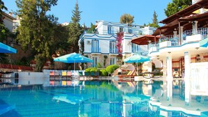 A swimming pool with lounge chairs and umbrellas, surrounded by buildings with balconies and a clear sky. - Soothe Hotel (Kas)