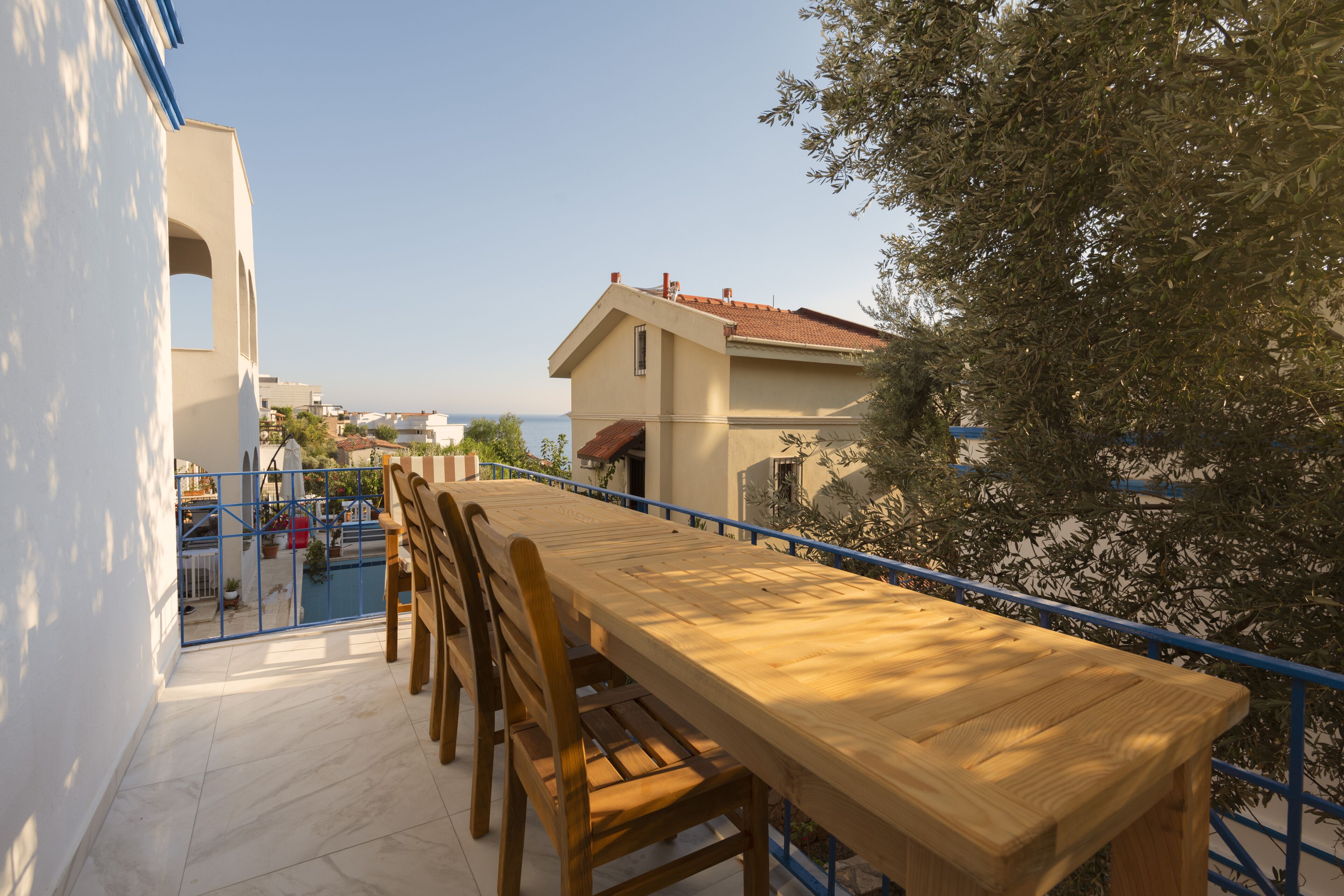 Una mesa de madera con sillas en un balcón, con vista al mar y un edificio con techo rojo.