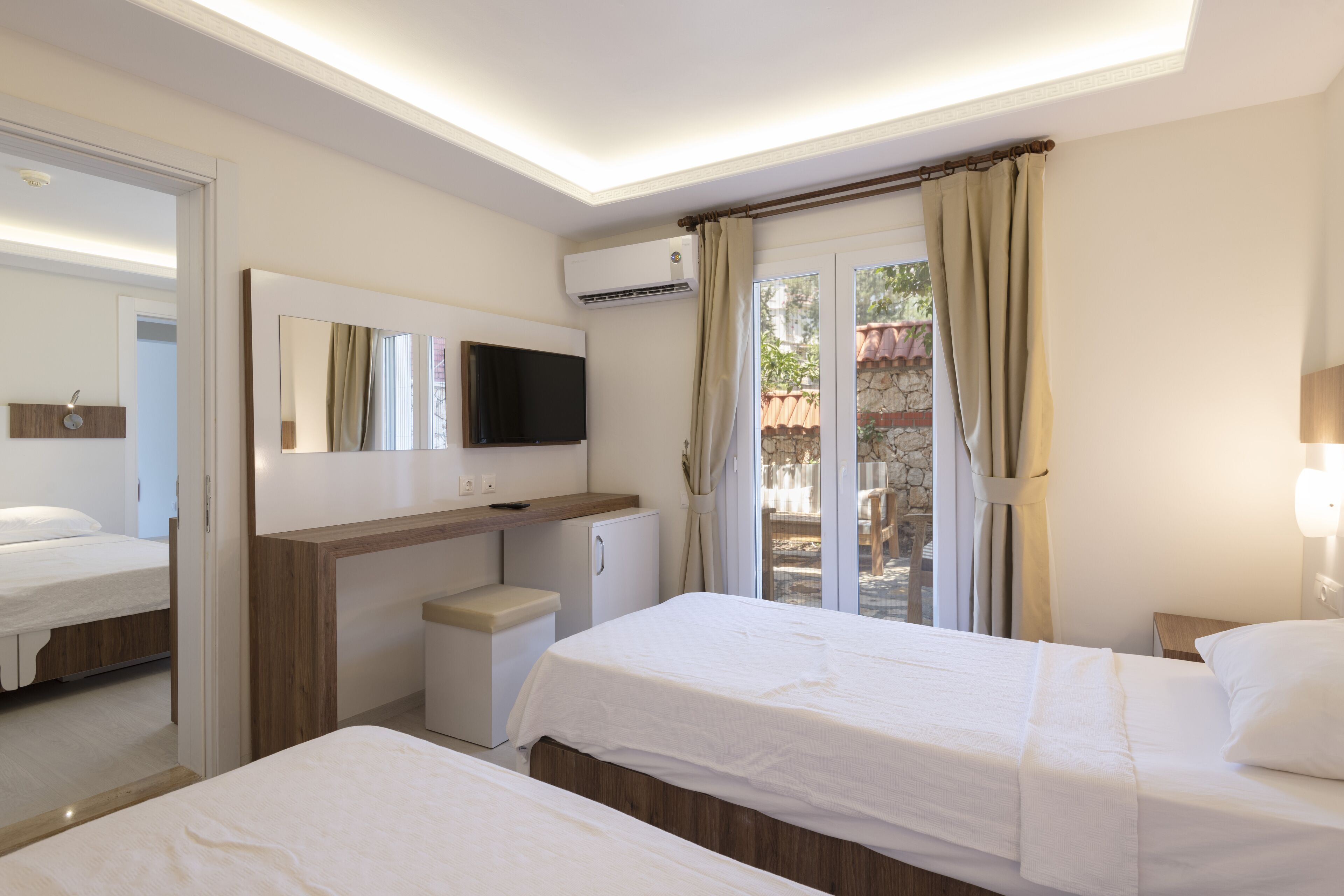 A hotel room with two beds, a TV, a desk, a small fridge, and a window with curtains.