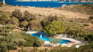 A pool with a wooden deck and lounge chairs, surrounded by trees and hills. - Ambelos (Malevizi)