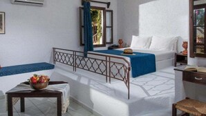 A room with a bed, a small table with a bowl of fruit, a chair, and a desk with a lamp. - Ambelos (Malevizi)