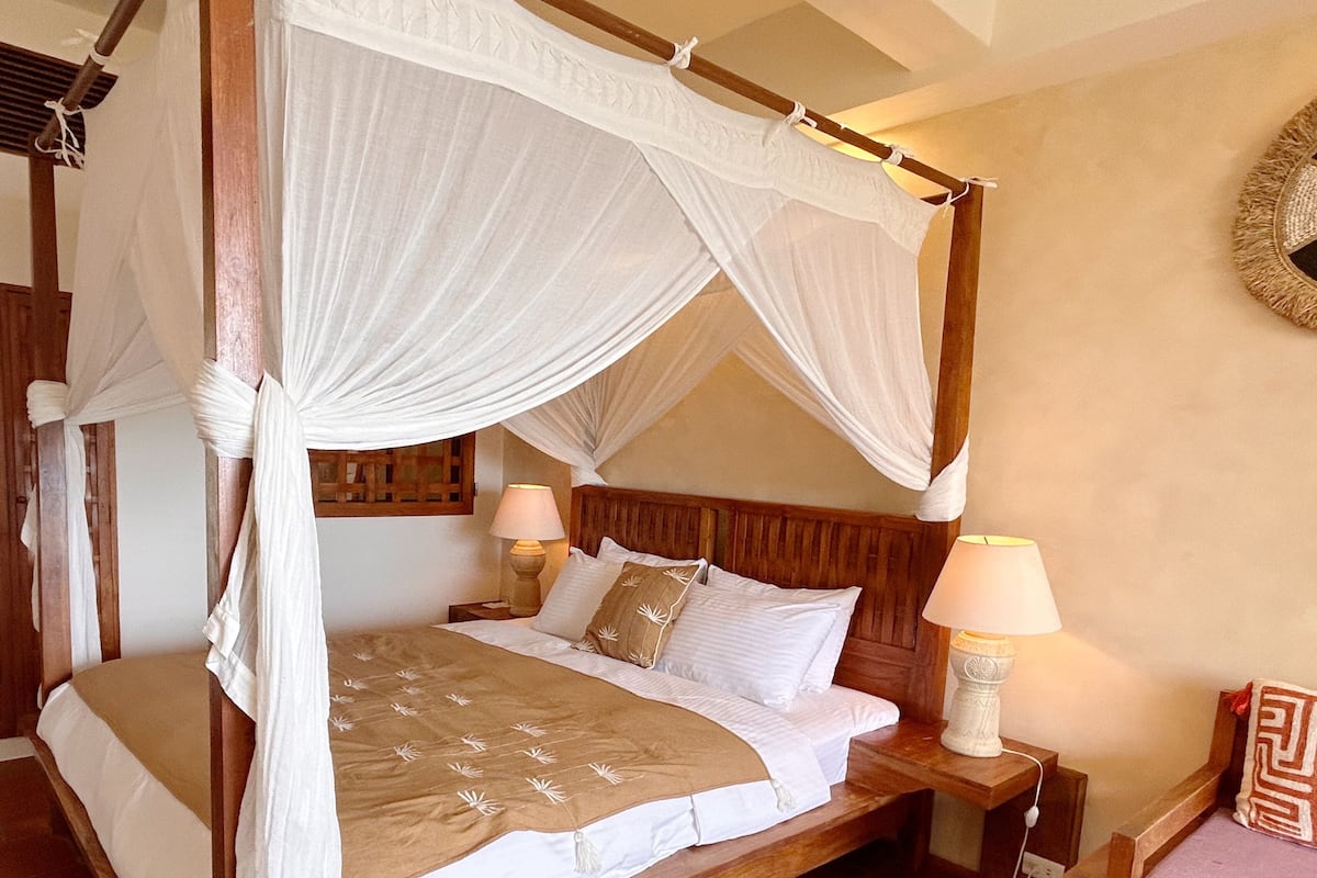 A four-poster canopy bed with white linens, two bedside lamps, and a wooden headboard.