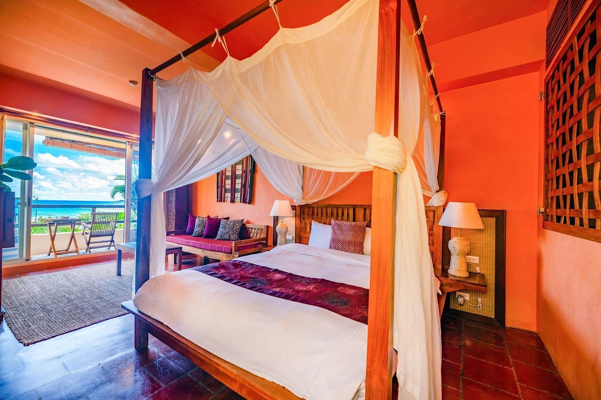 A four-poster bed with a canopy, a seating area with cushions, and a view of the ocean.