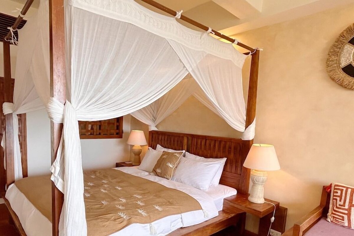 Una cama con dosel y cuatro columnas, con sábanas blancas, dos lámparas de noche y un cabecero de madera.