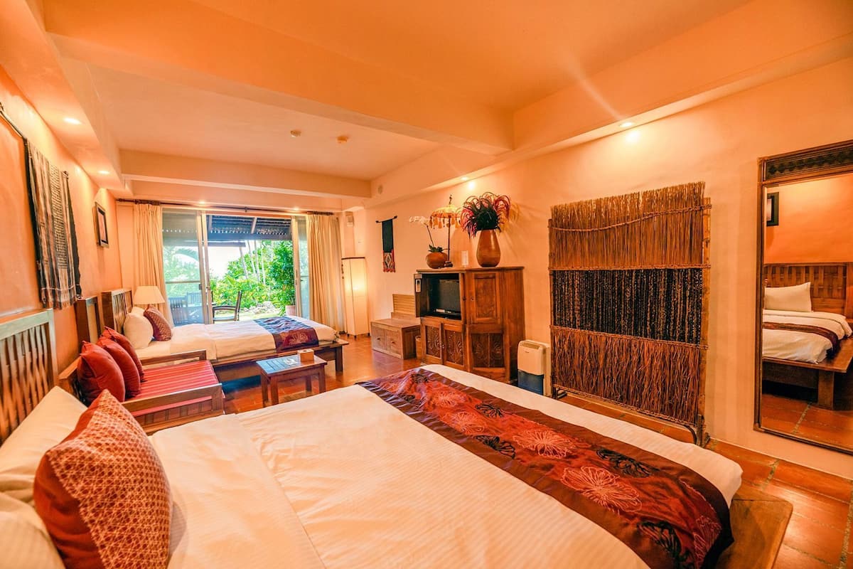 A hotel room with a large bed, a smaller bed, a desk, a TV, and a view of greenery outside.
