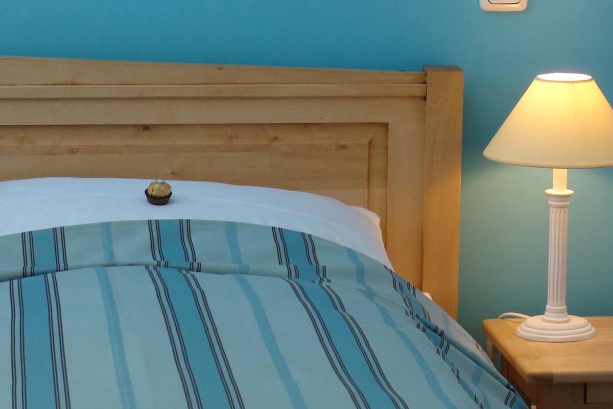 A bed with a striped blue and white bedspread, a wooden headboard, and a bedside table with a white lamp.