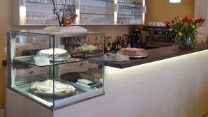 A bakery display case with pastries and a counter with a vase of flowers. - Landhaus Ribbeck (Nauen)