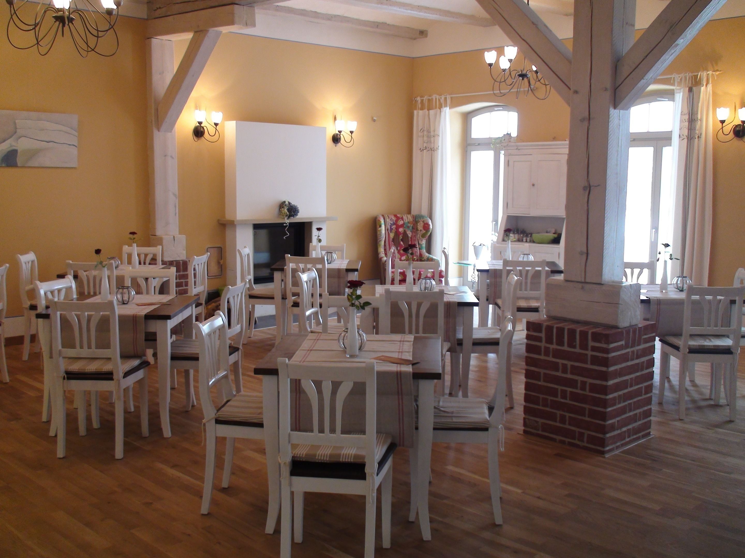Un comedor con sillas y mesas blancas, una chimenea de ladrillo y una cocina al fondo.