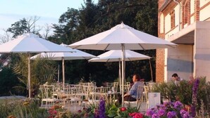 An outdoor seating area with white umbrellas and tables, surrounded by a variety of flowers. - Landhaus Ribbeck (Nauen)