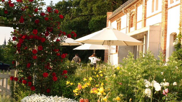 A garden with a variety of flowers and a building with a brick facade. - Landhaus Ribbeck (Nauen)