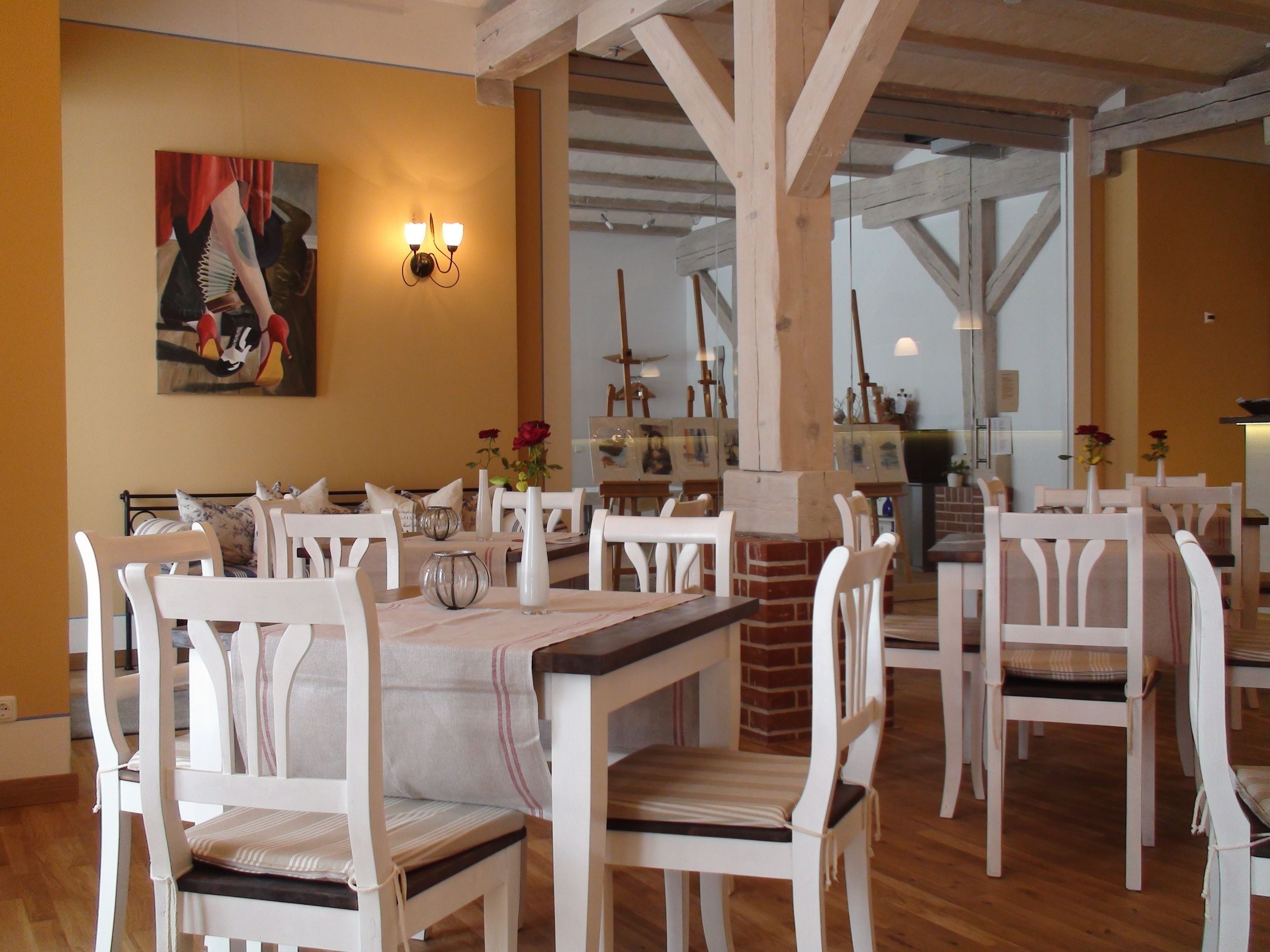 A dining area with white chairs and tables, a painting on the wall, and a brick fireplace.
